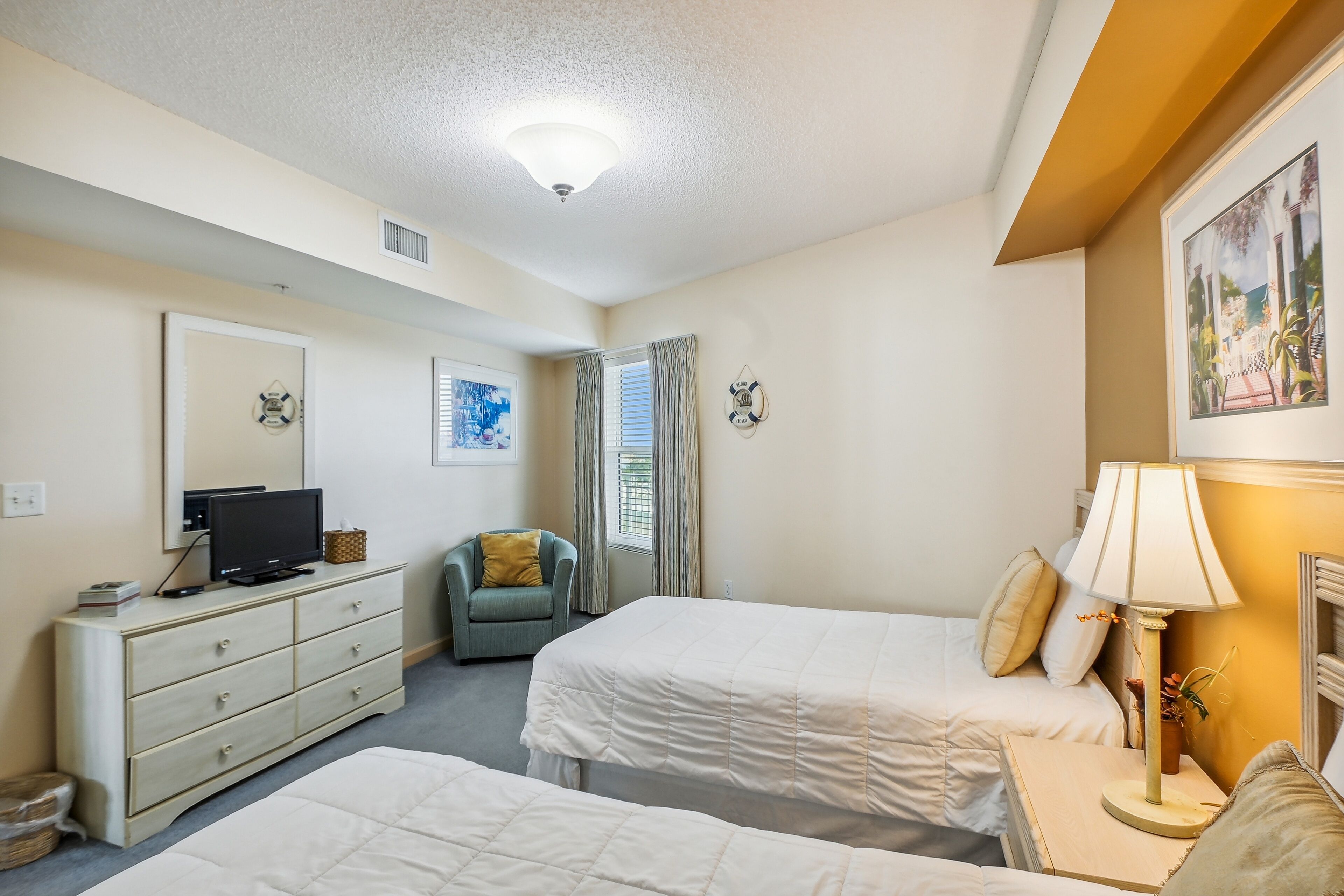 Une chambre d’hôtel avec deux lits, une commode, un téléviseur, une chaise et une lampe.