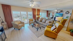 A spacious living room with a sofa, armchairs, a coffee table, and a TV. Large windows offer a view of the cityscape. - Seacrest 706 is a 2 BR Gulf Front on Okaloosa Island by RedAwning (Fort Walton Beach)