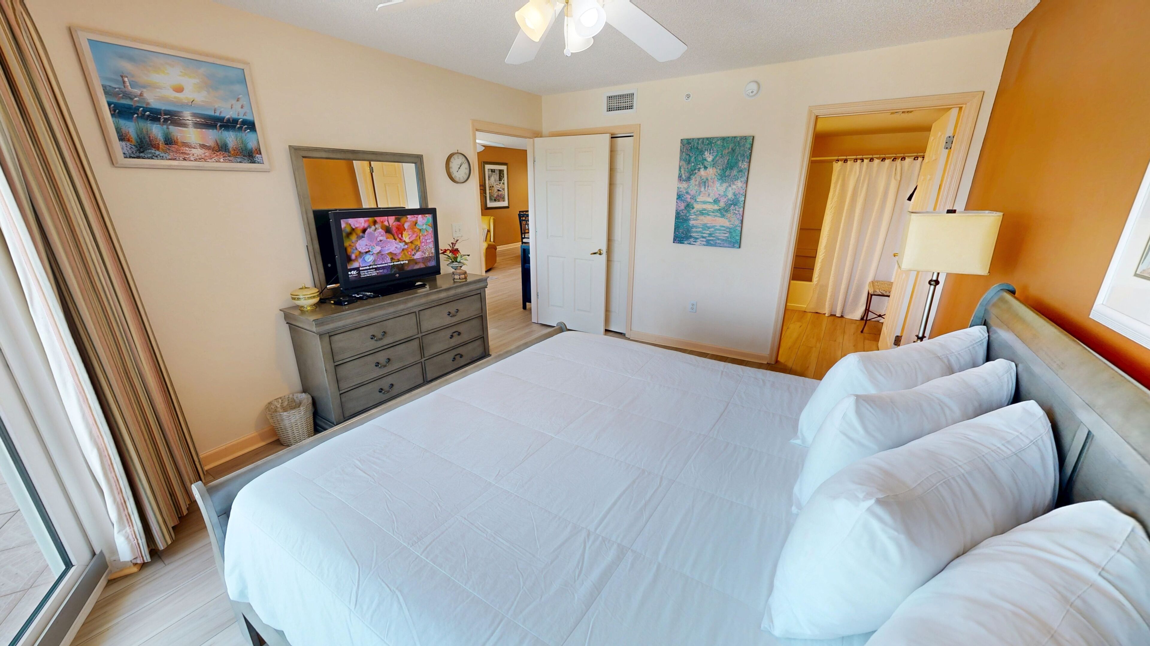 Camera d'albergo con un letto grande, una televisione su un comò, una ventola a soffitto e opere d'arte alle pareti.