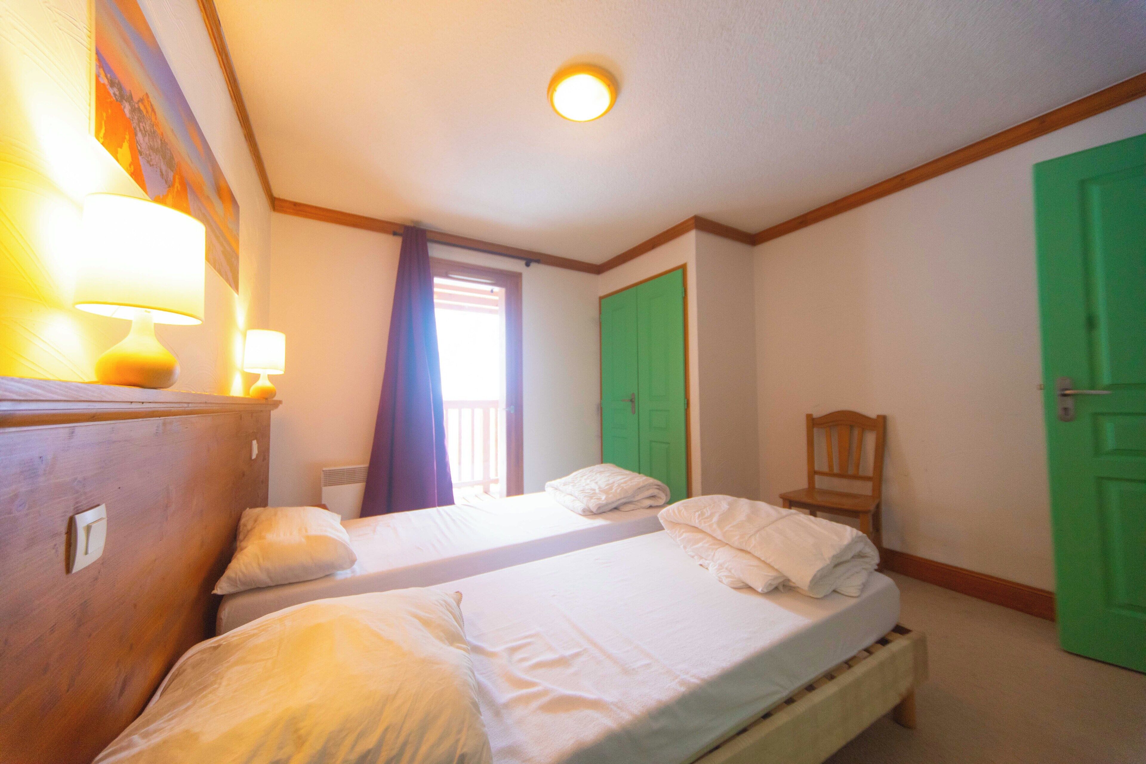 A bedroom with two beds, a wooden dresser, a chair, and a green door.