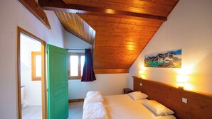 A bedroom with a wooden ceiling, a bed with white linens, a green door, and a painting on the wall. - Oz/Alpe d'Huez 110m slopes, up to 21 people, Hammam, en-suite bedrooms (Oz)