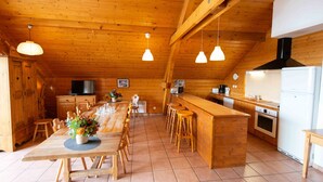 Tilava keittiö, jossa on puupalkit, pitkä ruokapöytä, baarituolit ja modernit kodinkoneet.