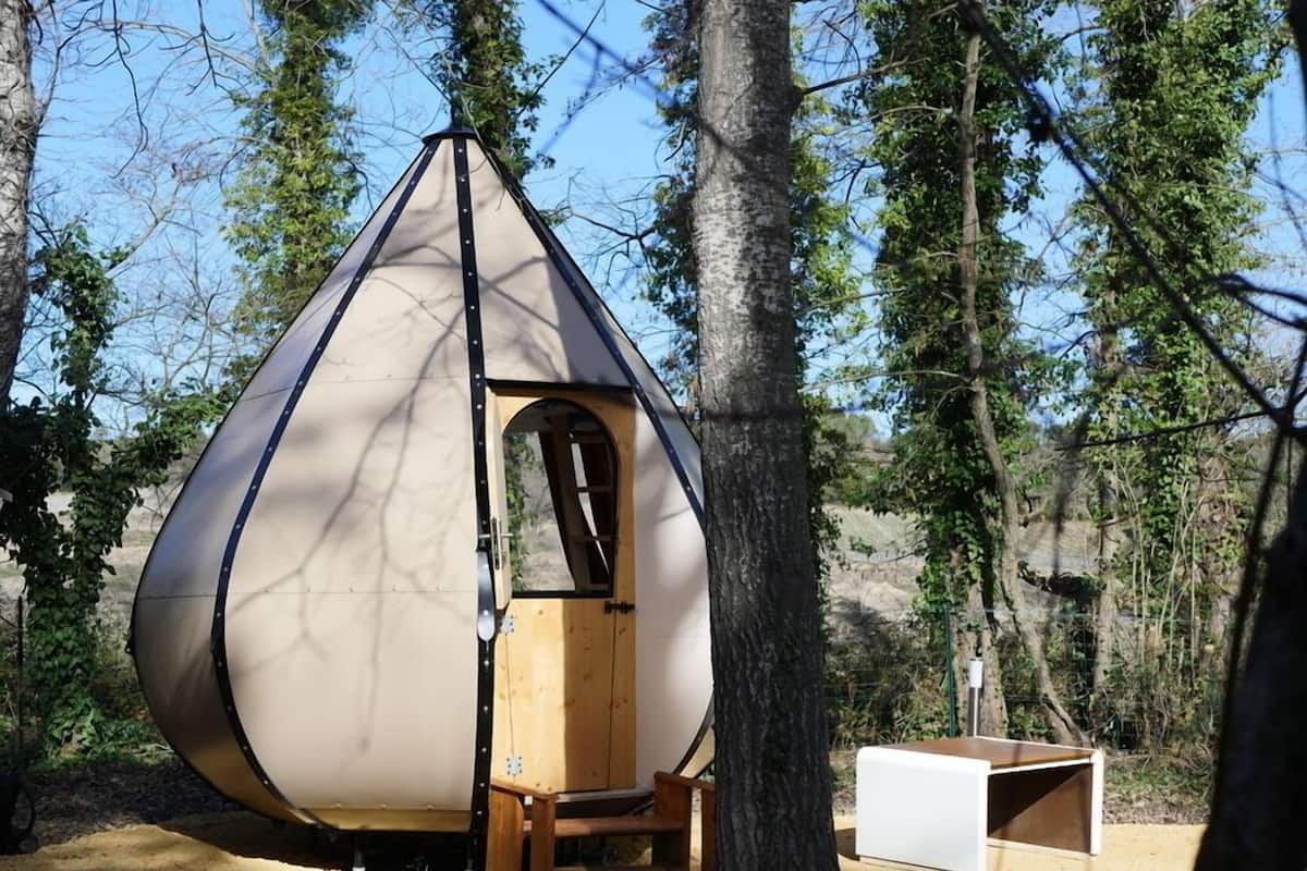 A geodesic dome structure with a wooden door and bench, surrounded by trees.