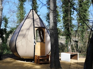 A geodesic dome structure with a wooden door and bench, surrounded by trees.
