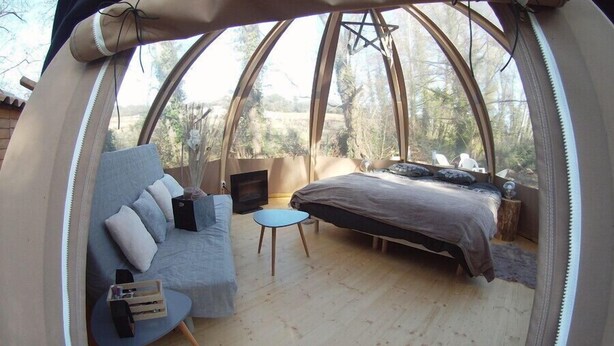 A cozy, circular tent-style room with a sofa, a small round table, a bed, and a television. - Nuit Etoilé (Mondragon)