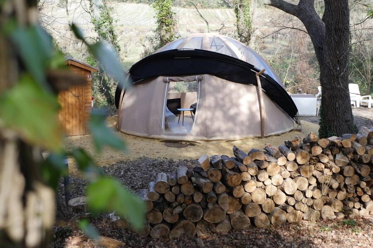 A dome-shaped tent with an open entrance, a small table, and chairs inside. A stack of firewood is in front of the tent.