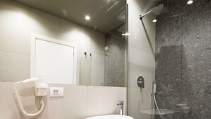 Un baño moderno con lavamanos blanco, cabina de ducha con paredes de vidrio y tocador de madera.