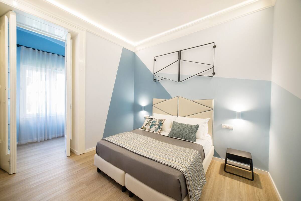 A modern bedroom with a bed, bedside table, and a geometric wall decoration.