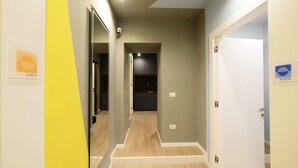 Un pasillo con suelo de madera, una puerta blanca a la derecha y un espejo a la izquierda.