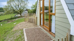 Una casa con techo inclinado, cerca de madera y patio cubierto de césped con ovejas.