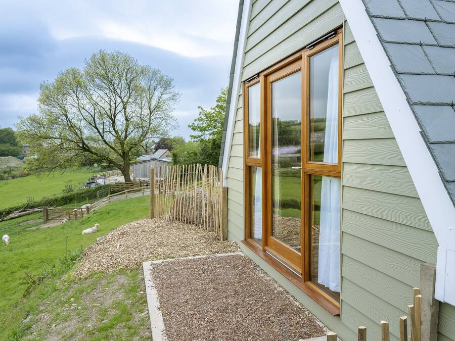 A house with a sloped roof, a wooden fence, and a grassy yard with sheep.