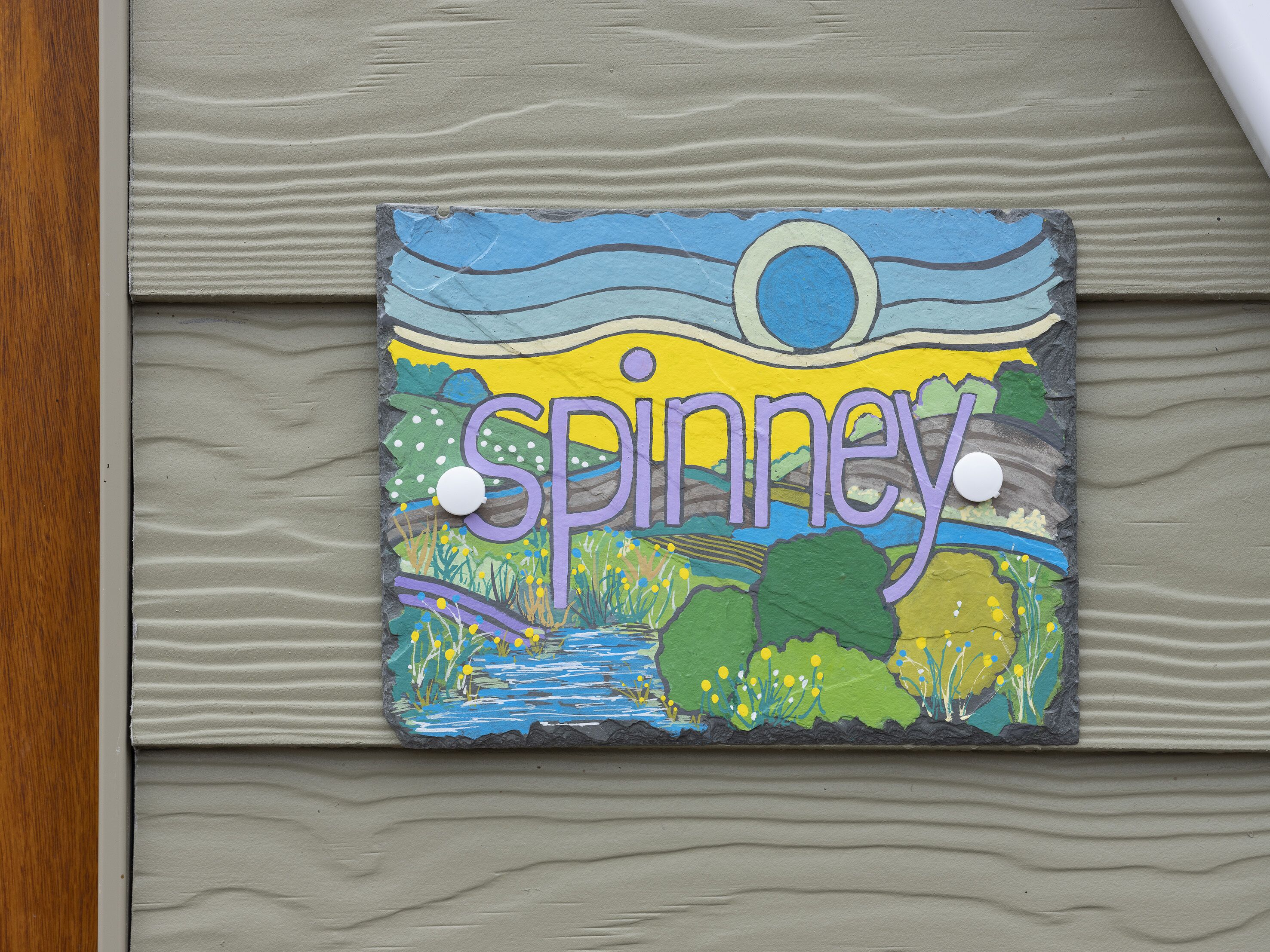 Un letrero decorativo con la palabra "Spinney" y una pintura de paisaje.