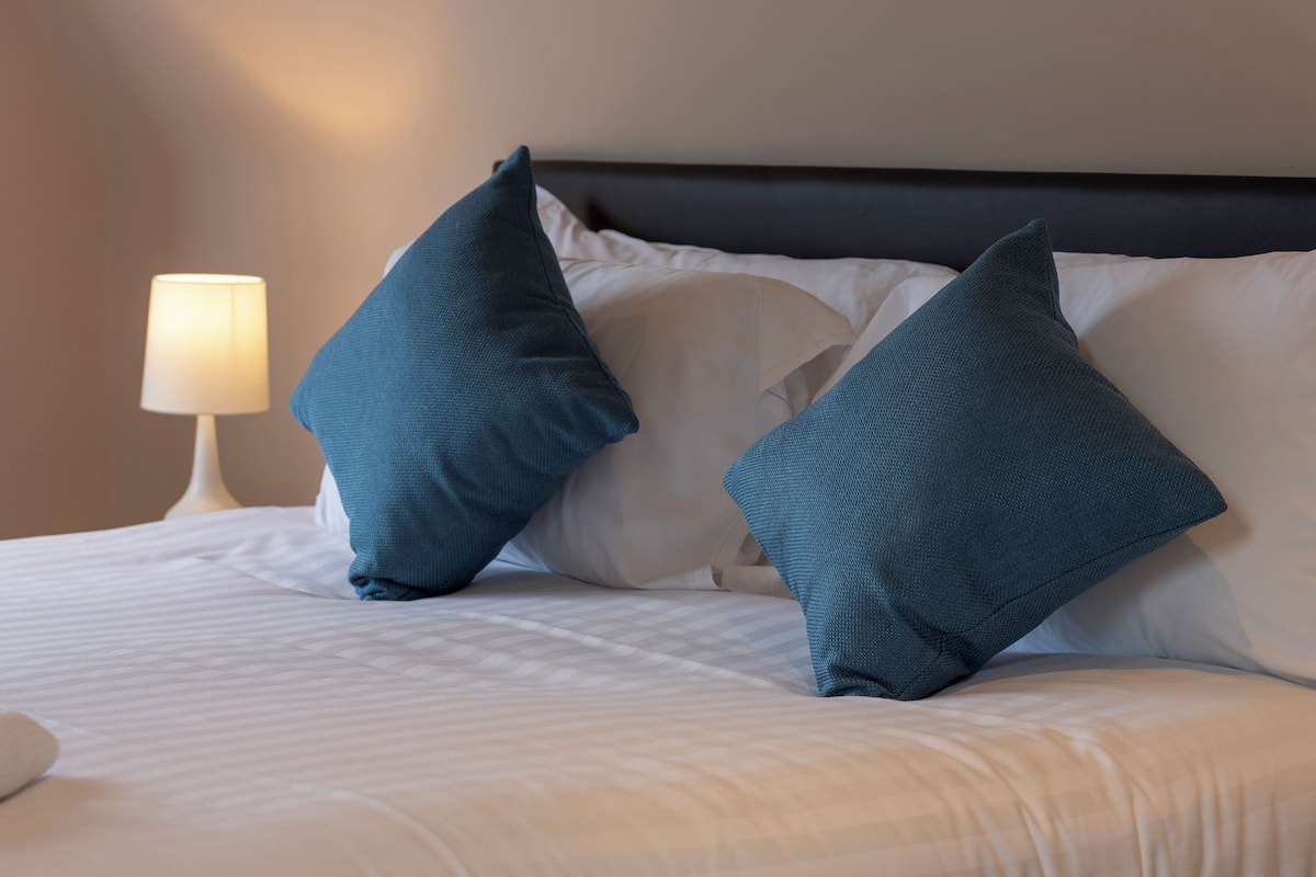 Una cama bien hecha con ropa blanca y dos almohadas color turquesa.