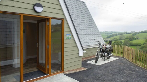Una casa con techo inclinado, una motocicleta estacionada afuera y vistas al campo.
