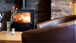 Un interior acogedor con una chimenea de piedra, una mesa con un florero y un sillón de cuero.