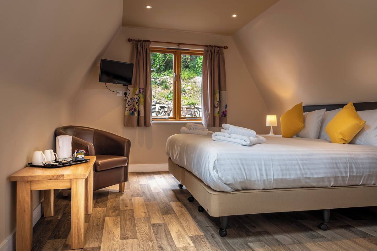 Una habitación de hotel con cama, escritorio, silla, televisor y ventana con cortinas.
