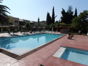 A swimming pool with lounge chairs and umbrellas, surrounded by trees and buildings.