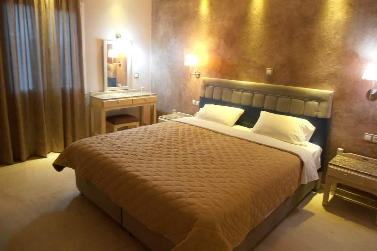 A hotel room with a large bed, a bedside table, a nightstand, a mirror, and a wall-mounted light.