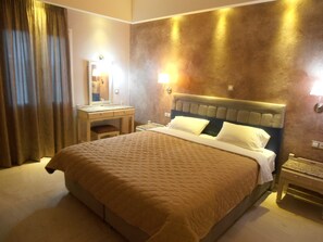 A hotel room with a large bed, a bedside table, a nightstand, a mirror, and a wall-mounted light. - Frosini Gardens (Corfu)