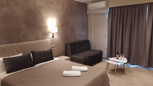 A modern hotel room with a large bed, two sofas, a small table with a bottle and glasses, and a window with curtains. - Frosini Gardens (Corfu)