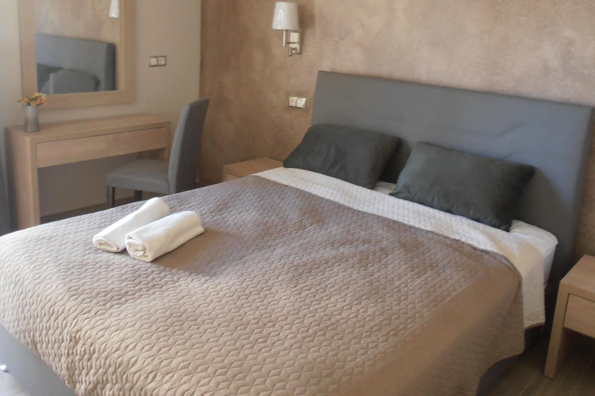 A neatly made bed with a quilted cover, a bedside lamp, and a wall-mounted mirror.