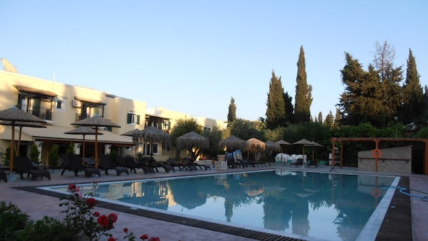 A swimming pool with lounge chairs and umbrellas, surrounded by buildings and trees. - Frosini Gardens (Corfu)