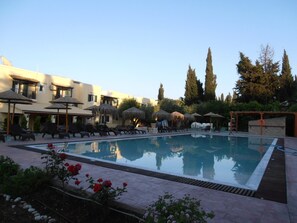 A swimming pool with lounge chairs and umbrellas, surrounded by buildings and trees.