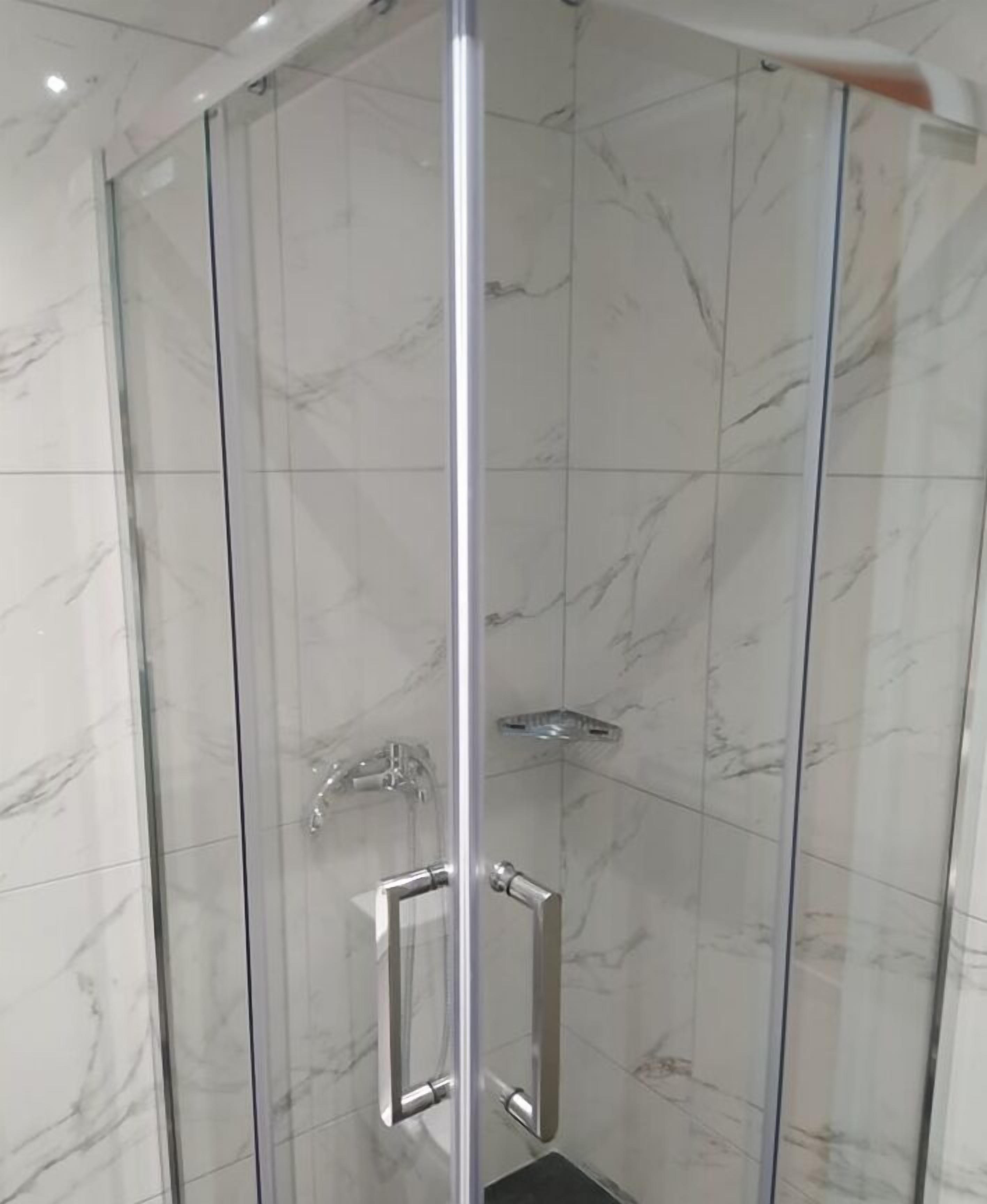 Een douche met glazen wanden, een chroomkleurige kraan en een handdouche.