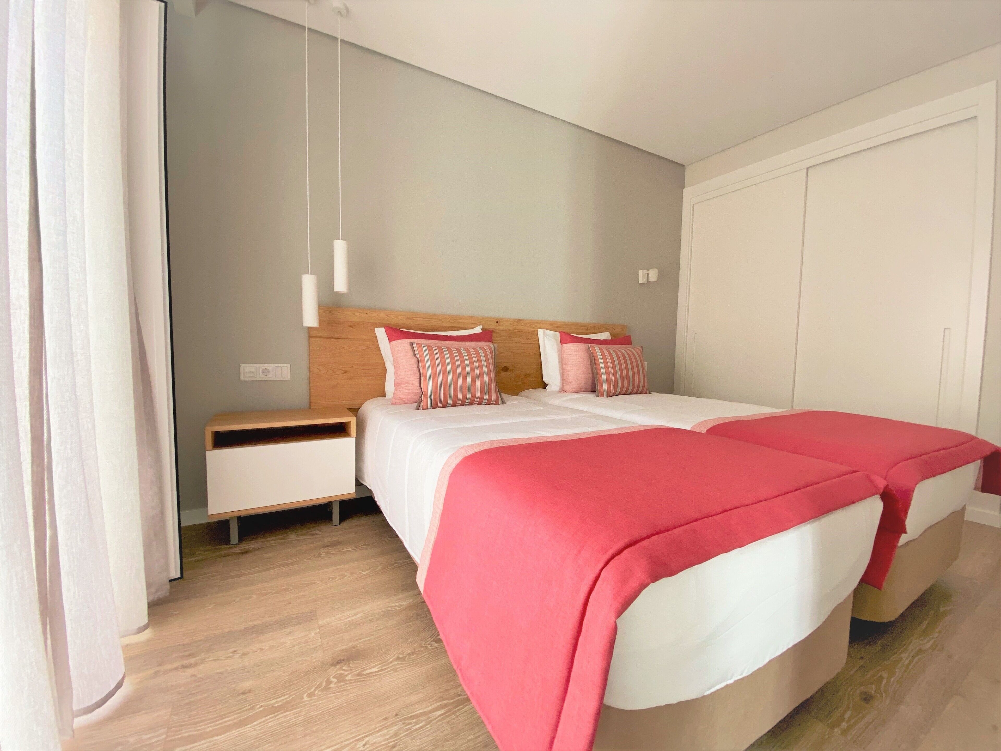 Un dormitorio con cabecera de madera, dos camas con ropa de cama rosa y blanca, una mesita de noche y una lámpara colgante.
