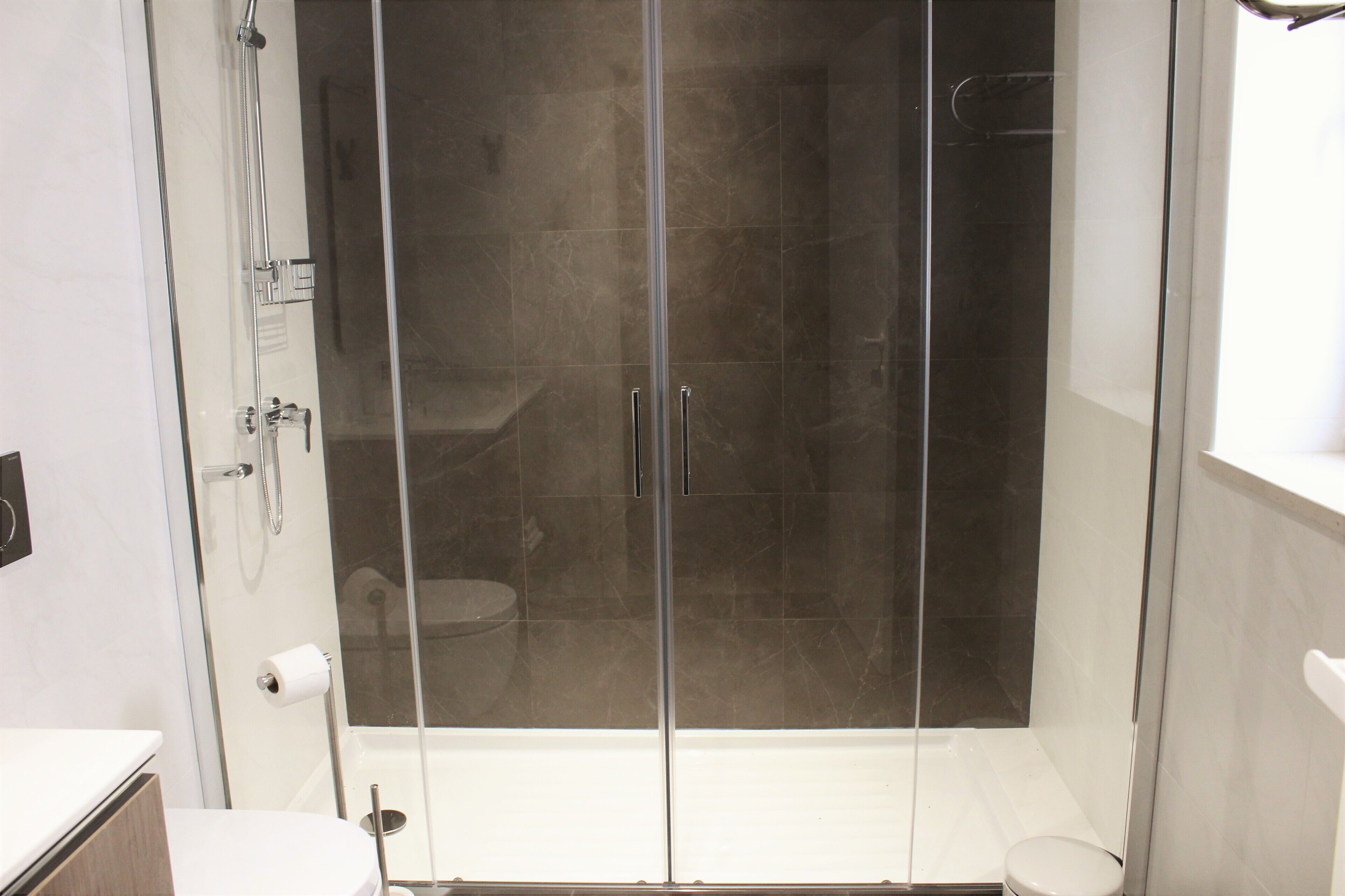 A modern bathroom with a glass-enclosed shower, a white sink, and a toilet.