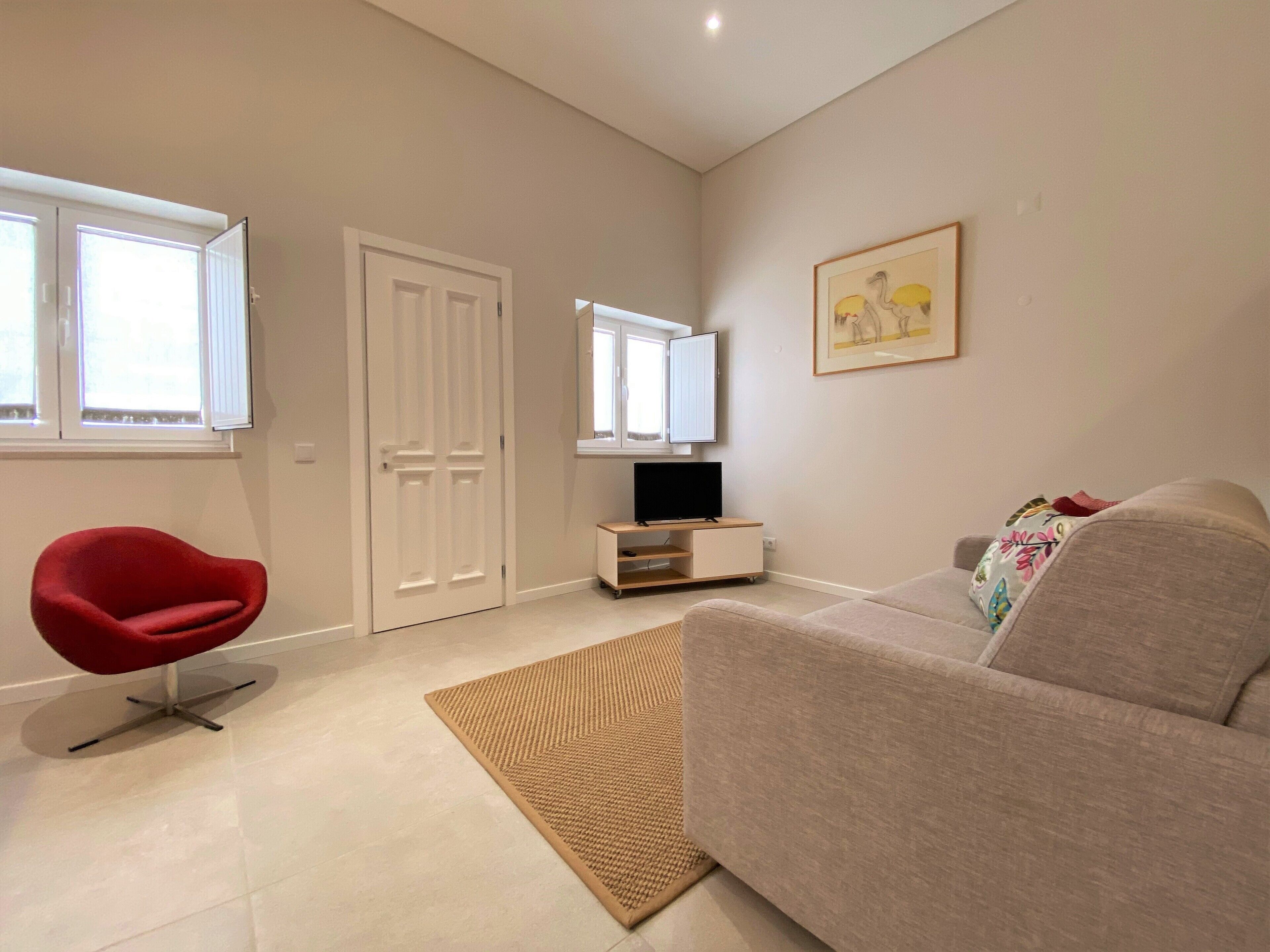 A living room with a red chair, a beige sofa, a TV stand, and a framed picture on the wall.