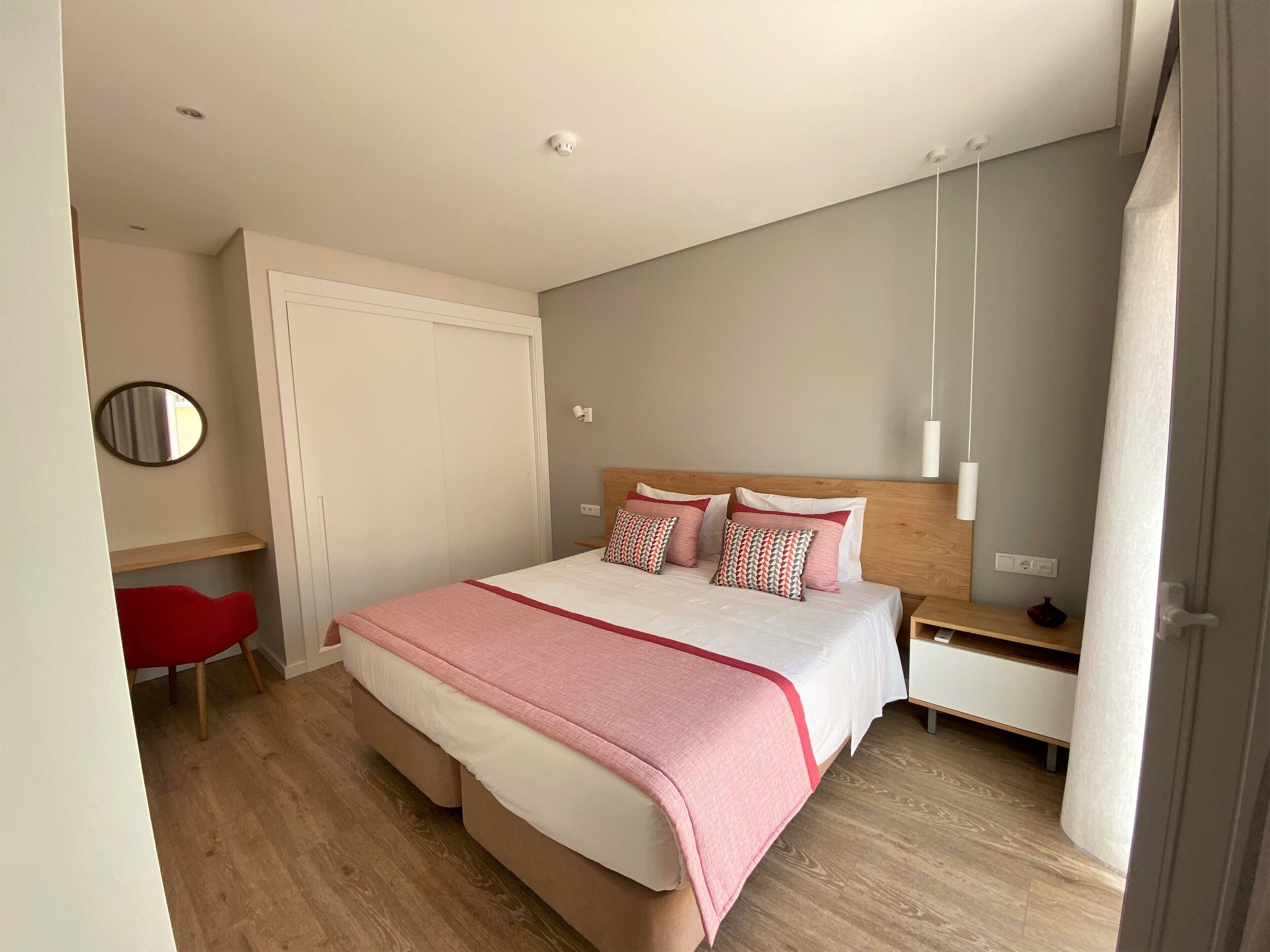 Une chambre moderne avec un grand lit, des tables de chevet, un miroir et un fauteuil rouge.