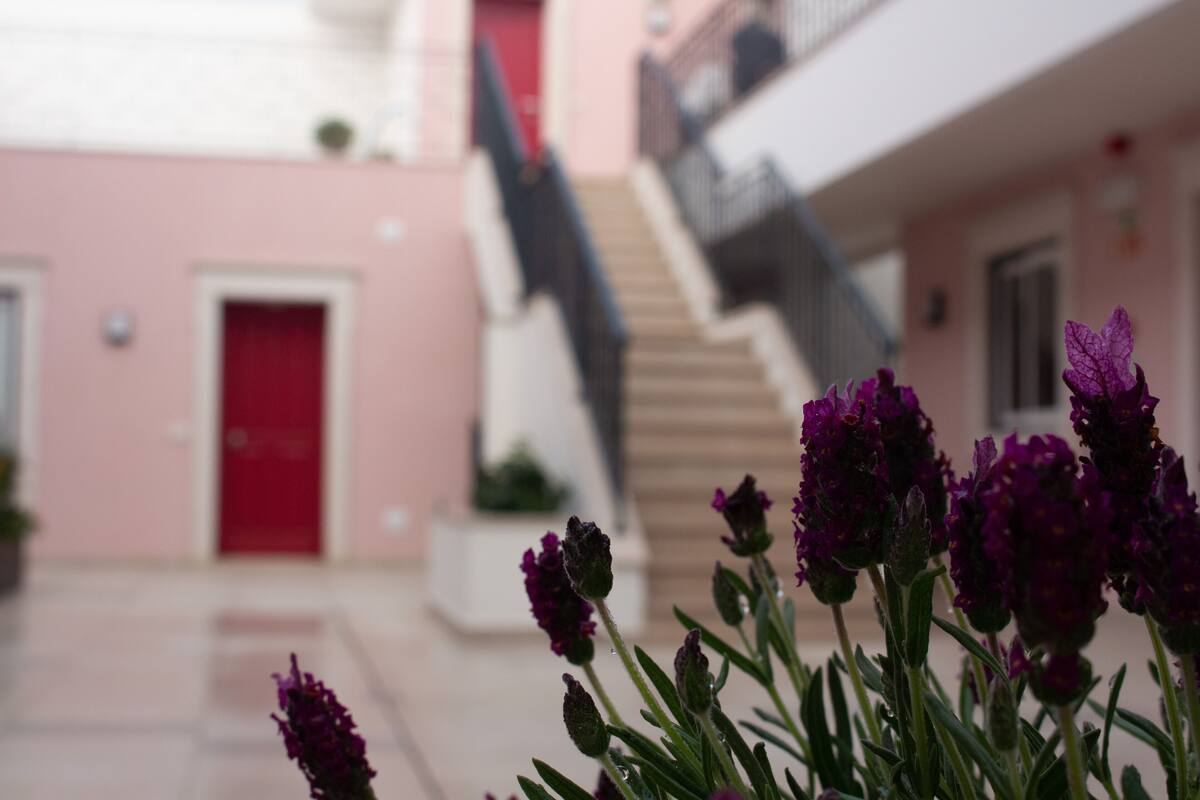 A building with a pink facade, a red door, and a staircase leading to an upper level.