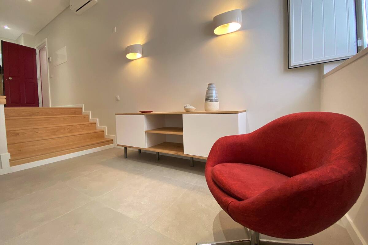 A modern interior with a red chair, a staircase, and a wall-mounted shelf with decorative items.