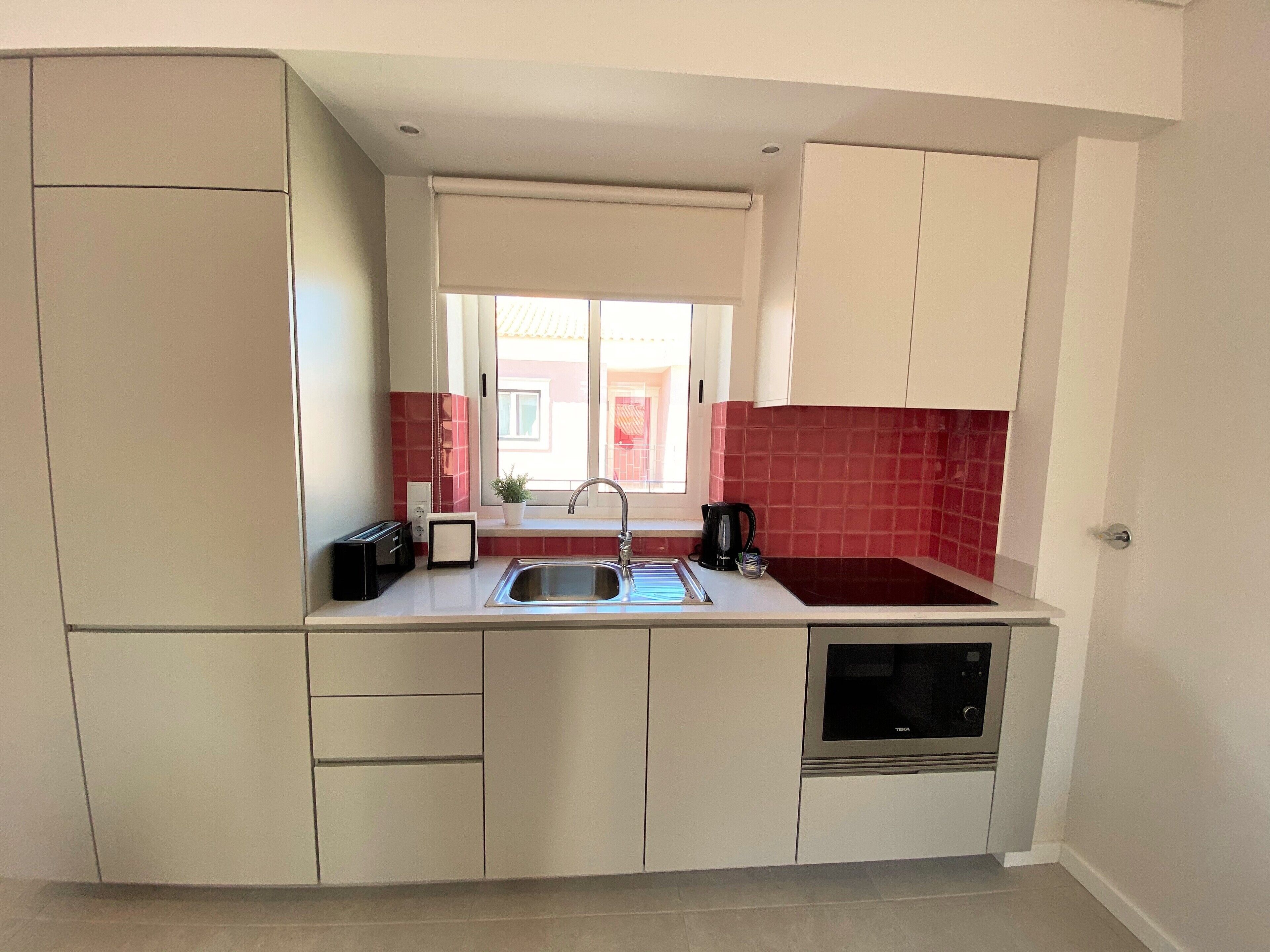 Una cocina compacta con lavamanos, tostadora, hervidor y horno empotrado.