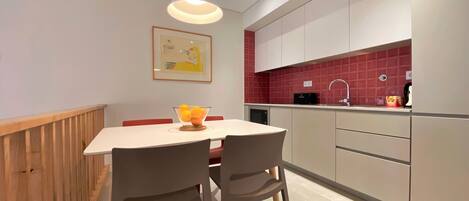 A modern kitchen with a dining table, chairs, a hanging light fixture, and a red-tiled backsplash.