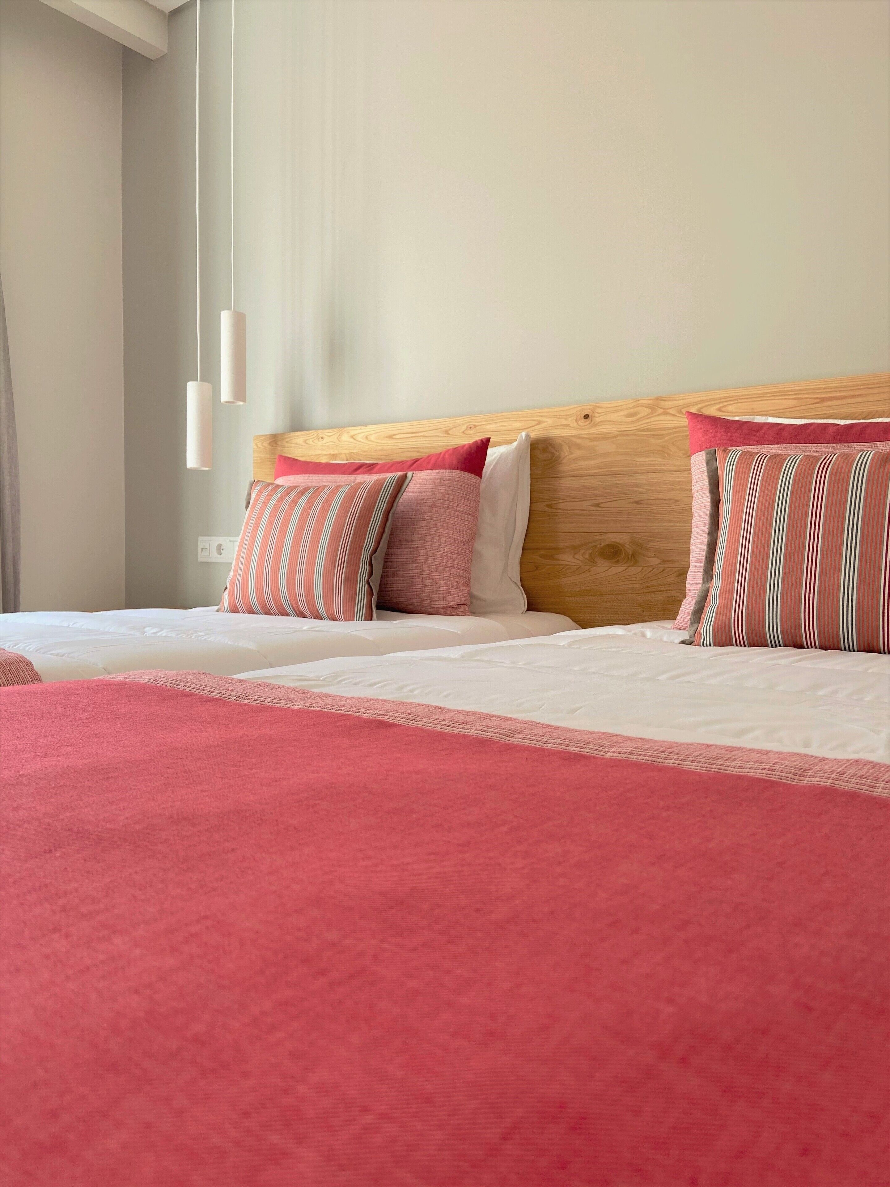 A hotel room with a wooden headboard, two beds with white bedding, and pink and striped pillows.