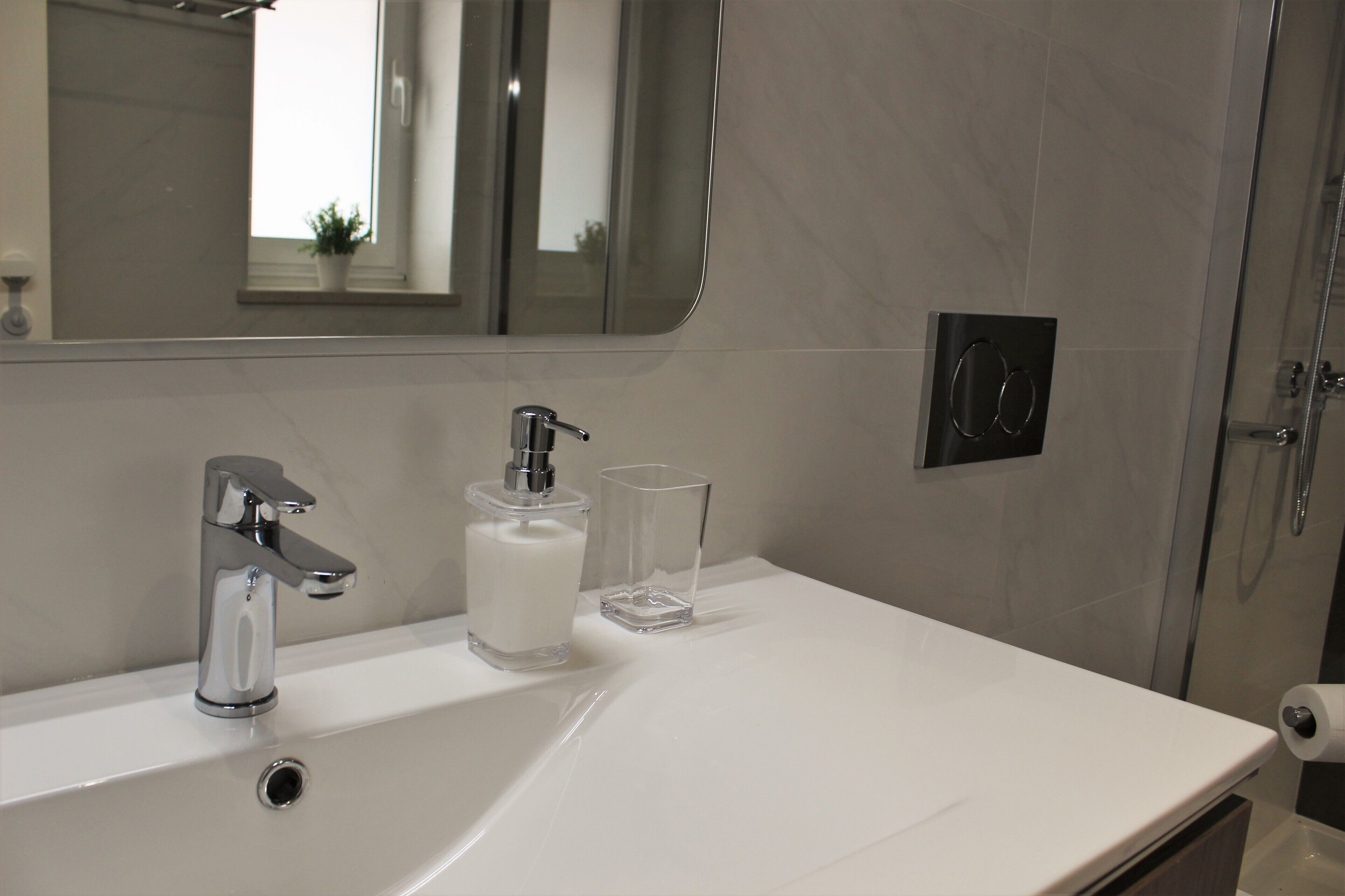 A modern bathroom with a white sink, chrome faucet, and a glass bottle of soap.
