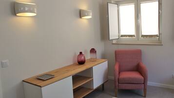 Ein Zimmer mit einem Holztisch, zwei Wandleuchten, einem rot gemusterten Stuhl, einem Fenster mit Jalousien und einem kleinen Teppich auf dem Boden.