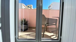 A sliding glass door leading to an outdoor patio with a potted plant and a metal chair. - Cardeal Suites & Apartments (Faro)