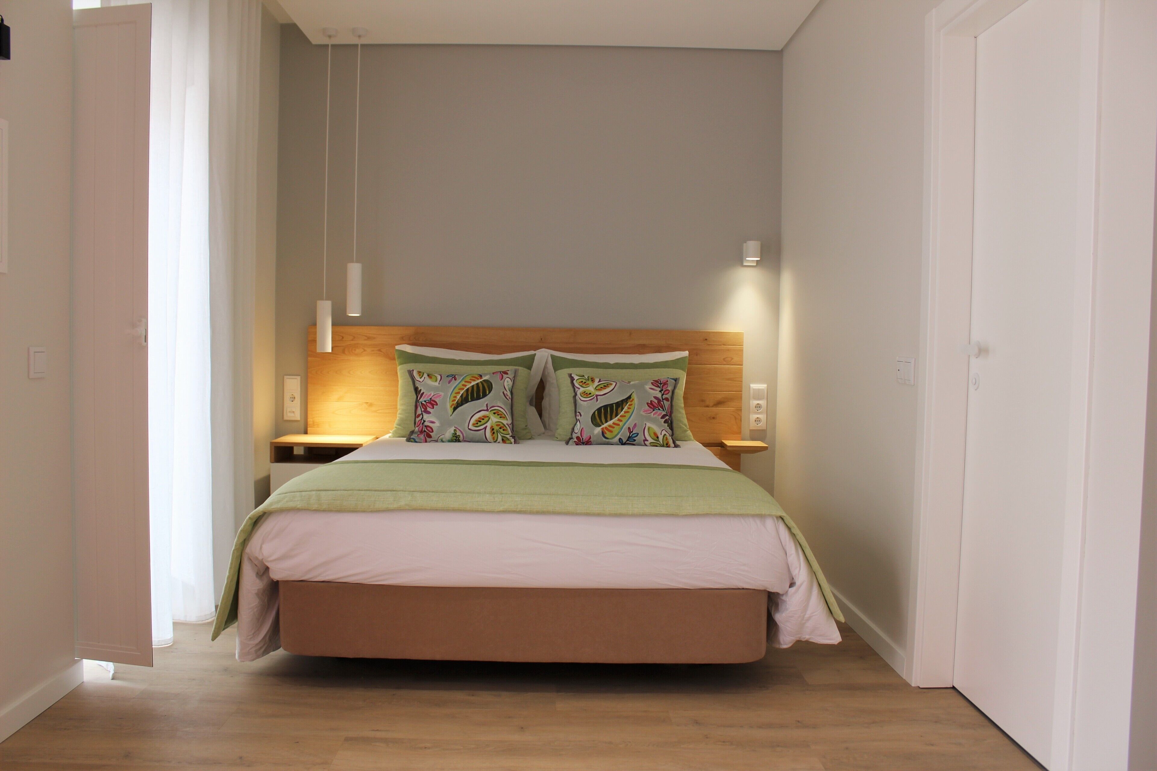 Ein Schlafzimmer mit hölzernem Kopfteil, zwei Nachttischen, einem Bett mit grüner Decke und einer weißen Wand mit einer Lampe.