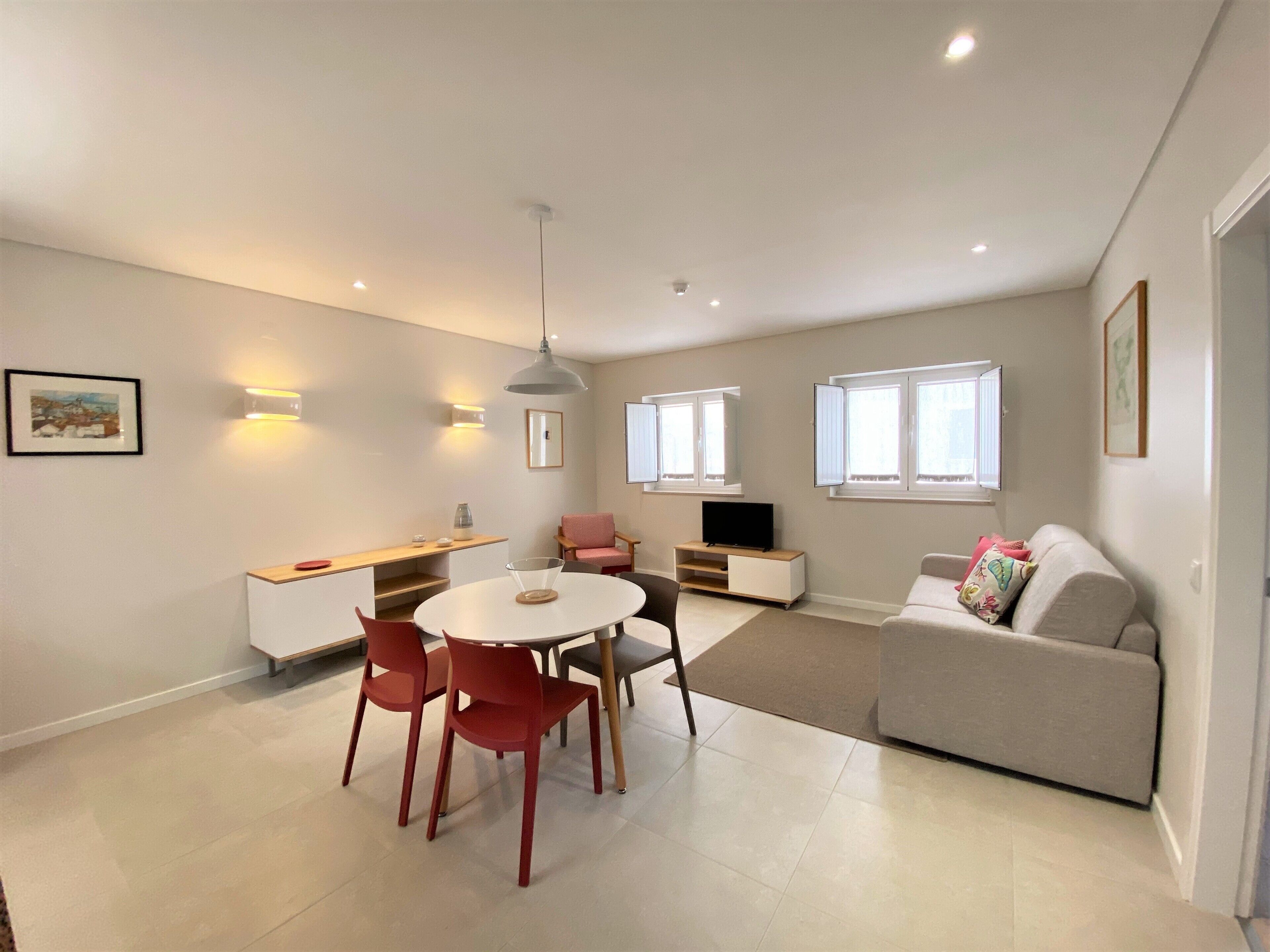 A modern living room with a dining area, a sofa, a TV, and a window with curtains.