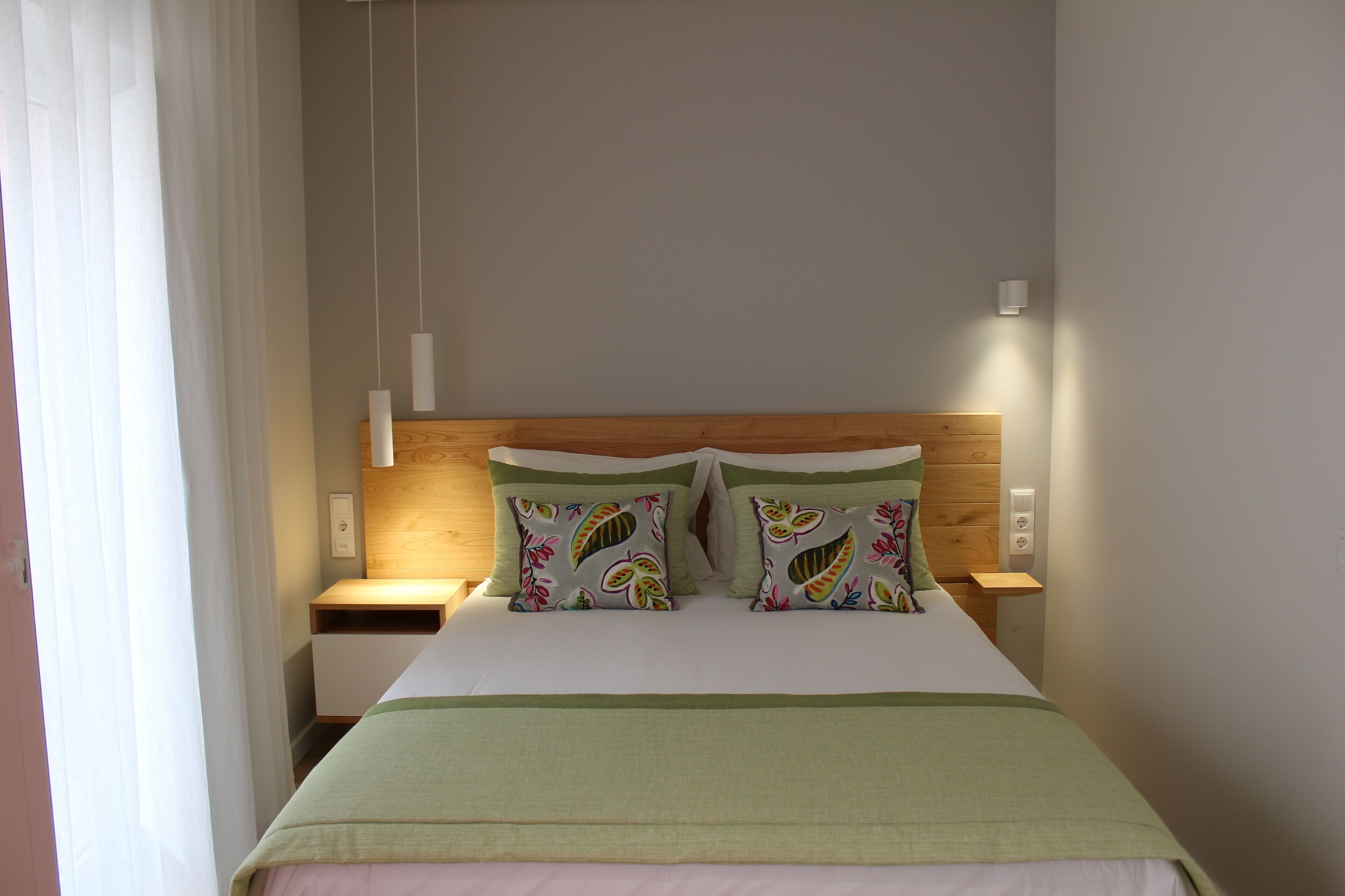 A hotel room with a bed, two nightstands, a wooden headboard, and a window with curtains.