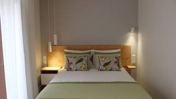 A hotel room with a bed, two nightstands, a wooden headboard, and a window with curtains.