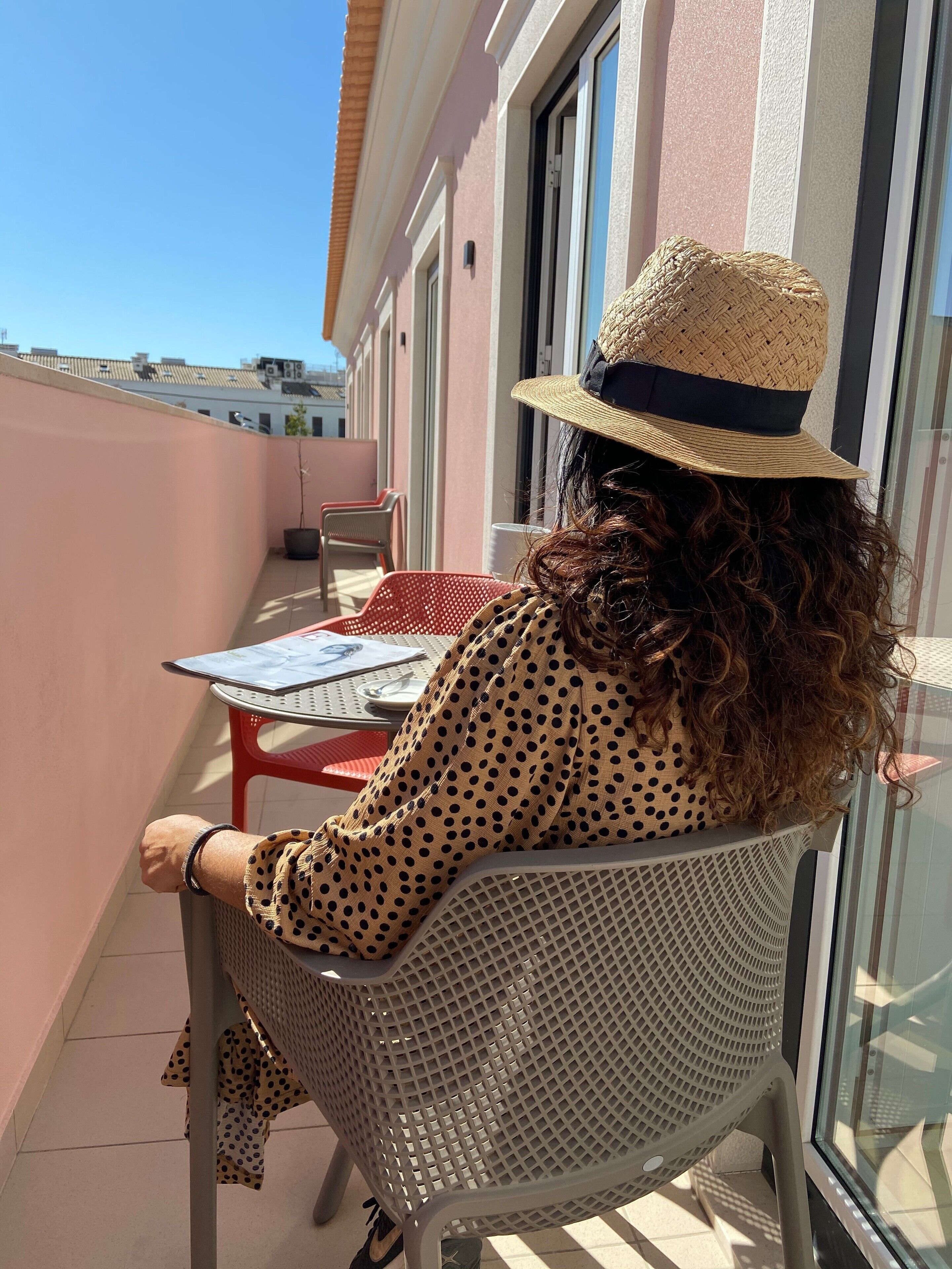 Uma pessoa sentada à mesa em uma varanda com vista para edifícios.