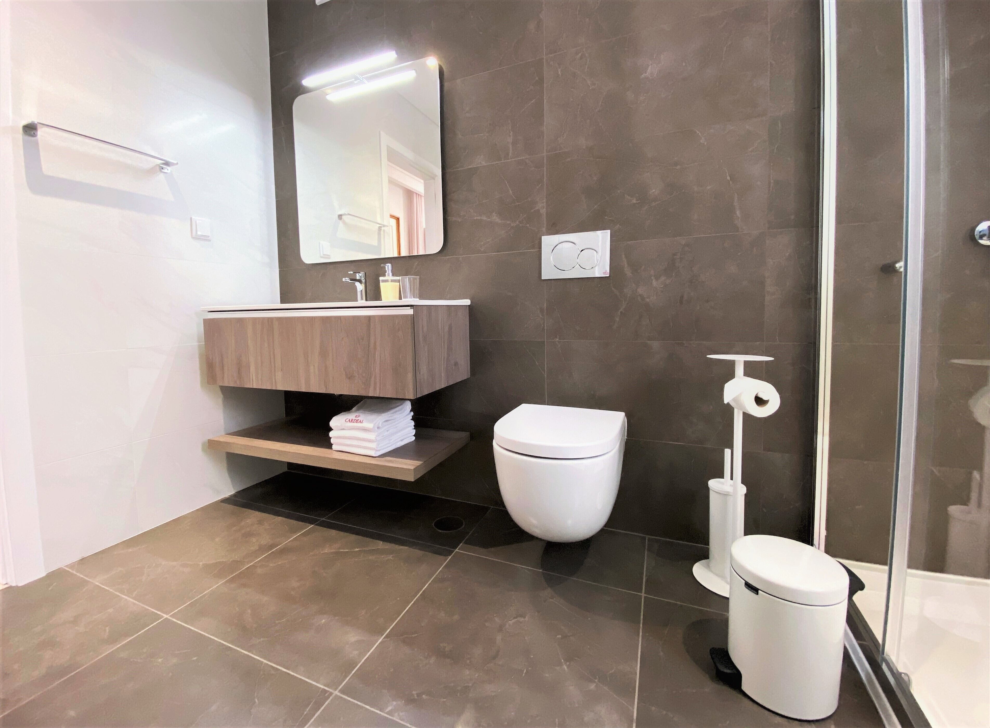 A modern bathroom with a wooden vanity, a white toilet, and a glass shower enclosure.