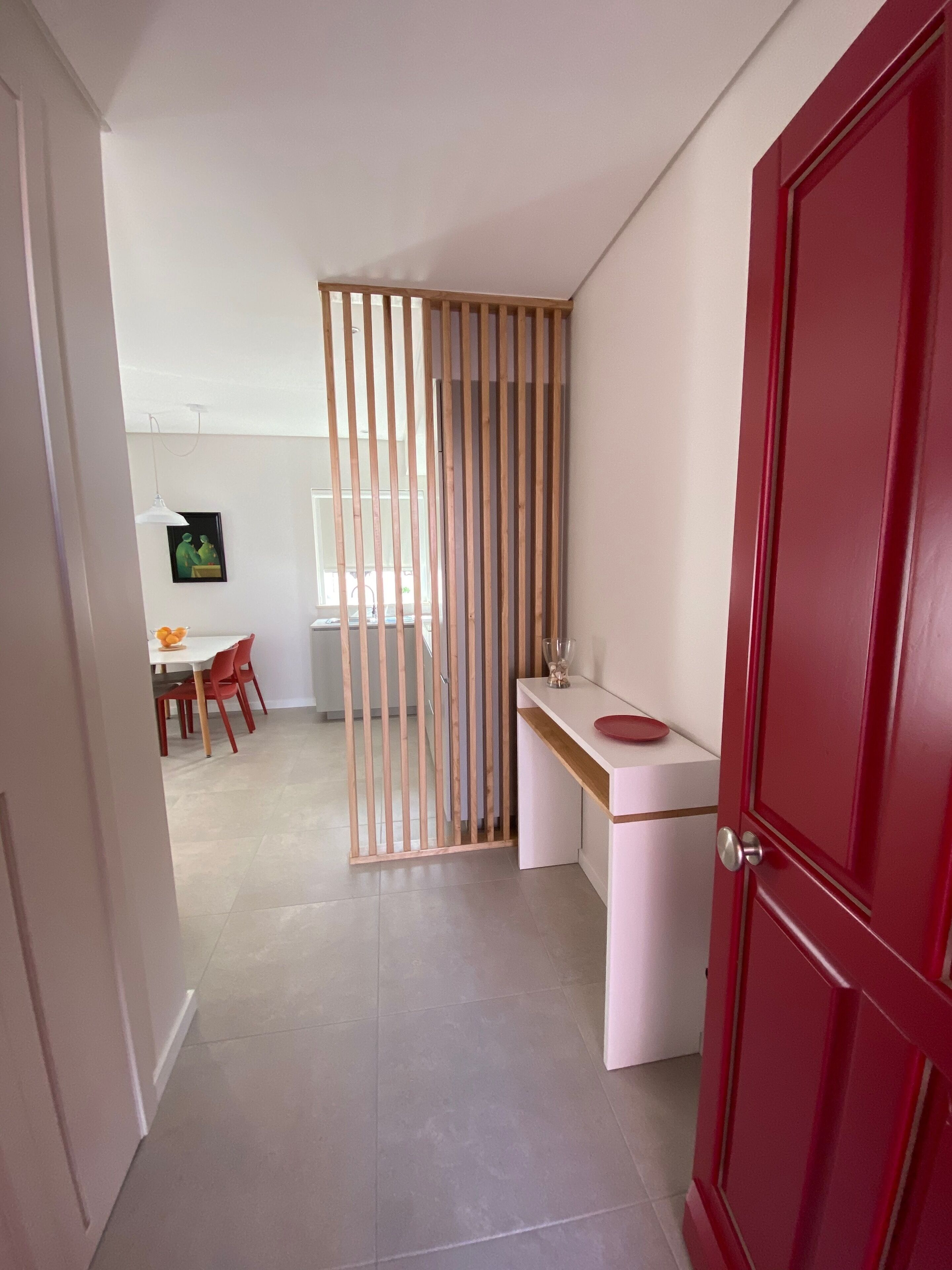 A modern kitchen with a white countertop, a red door, and a dining area with a white table and red chairs.