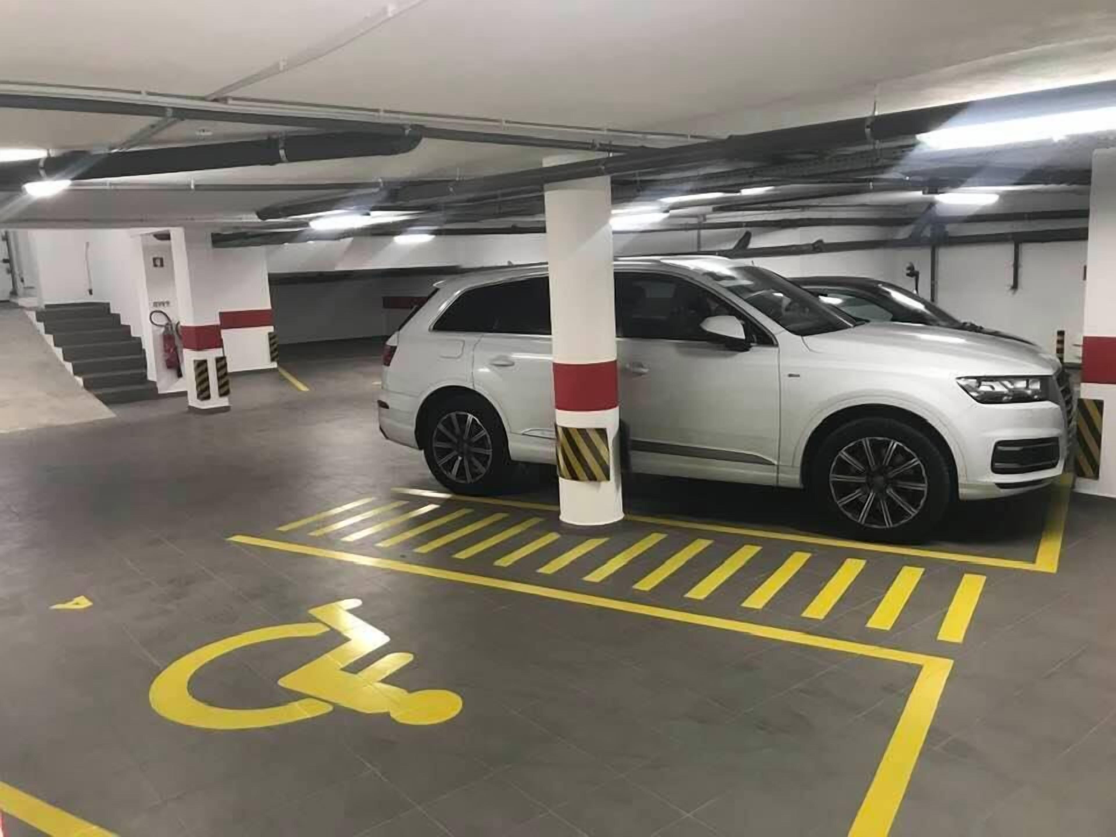 Eine Parkgarage mit weißen Autos in markierten Stellplätzen, darunter ein Stellplatz für Menschen mit Behinderung.