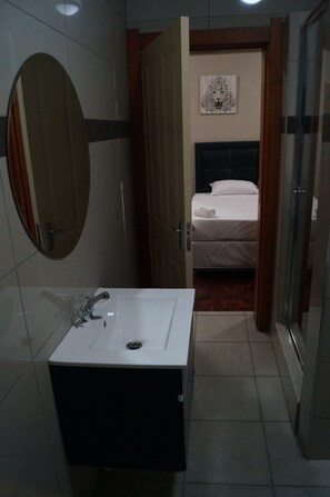 A bathroom with a white sink, a mirror, and a bed visible through an open door.