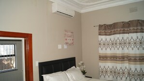 Hotelkamer met een bed, een raam met tralies, een airconditioning, een decoratief wandobject en een gordijn met een patroon.